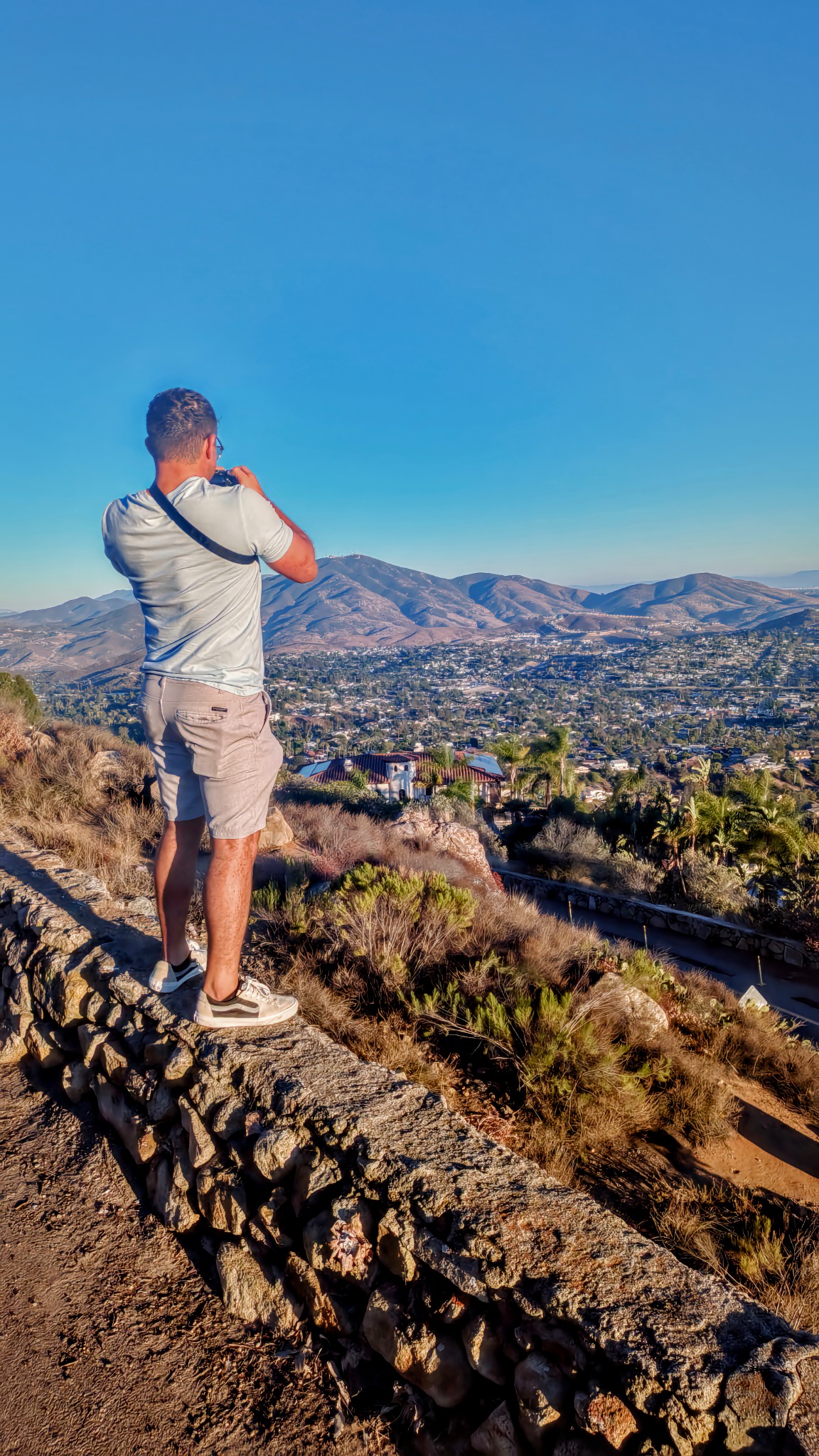 Hermz photographing a Southern California valley from a stone overlook, camera raised to his eye.