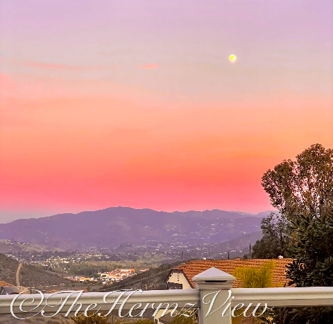 A vibrant pink, orange, and purple sunset sky with a bright moon hanging over distant mountains and a valley neighborhood.