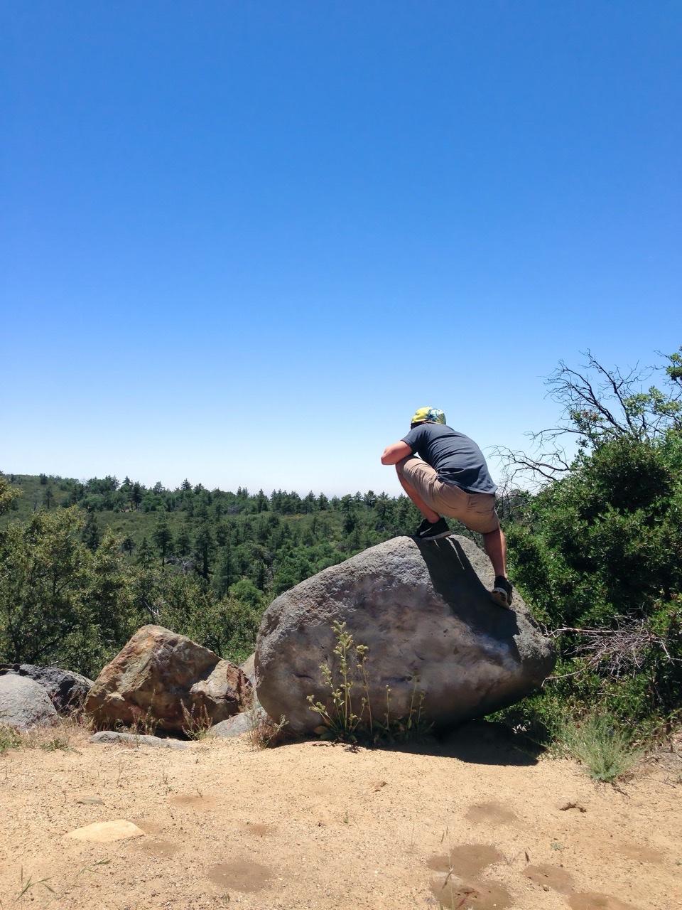 Hermz Shamoun perched on a granite boulder above pine-covered ridges