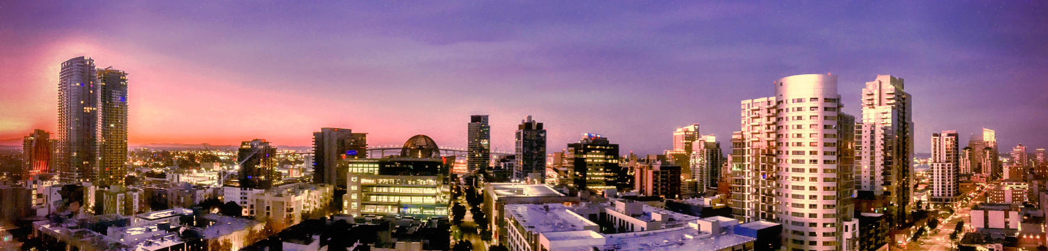 Panoramic view of a city skyline with illuminated buildings under a gradient purple and pink twilight sky.