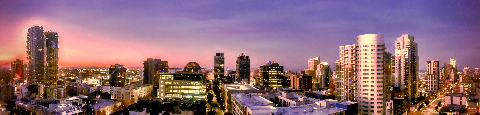 Panoramic view of a city skyline with illuminated buildings under a gradient purple and pink twilight sky.