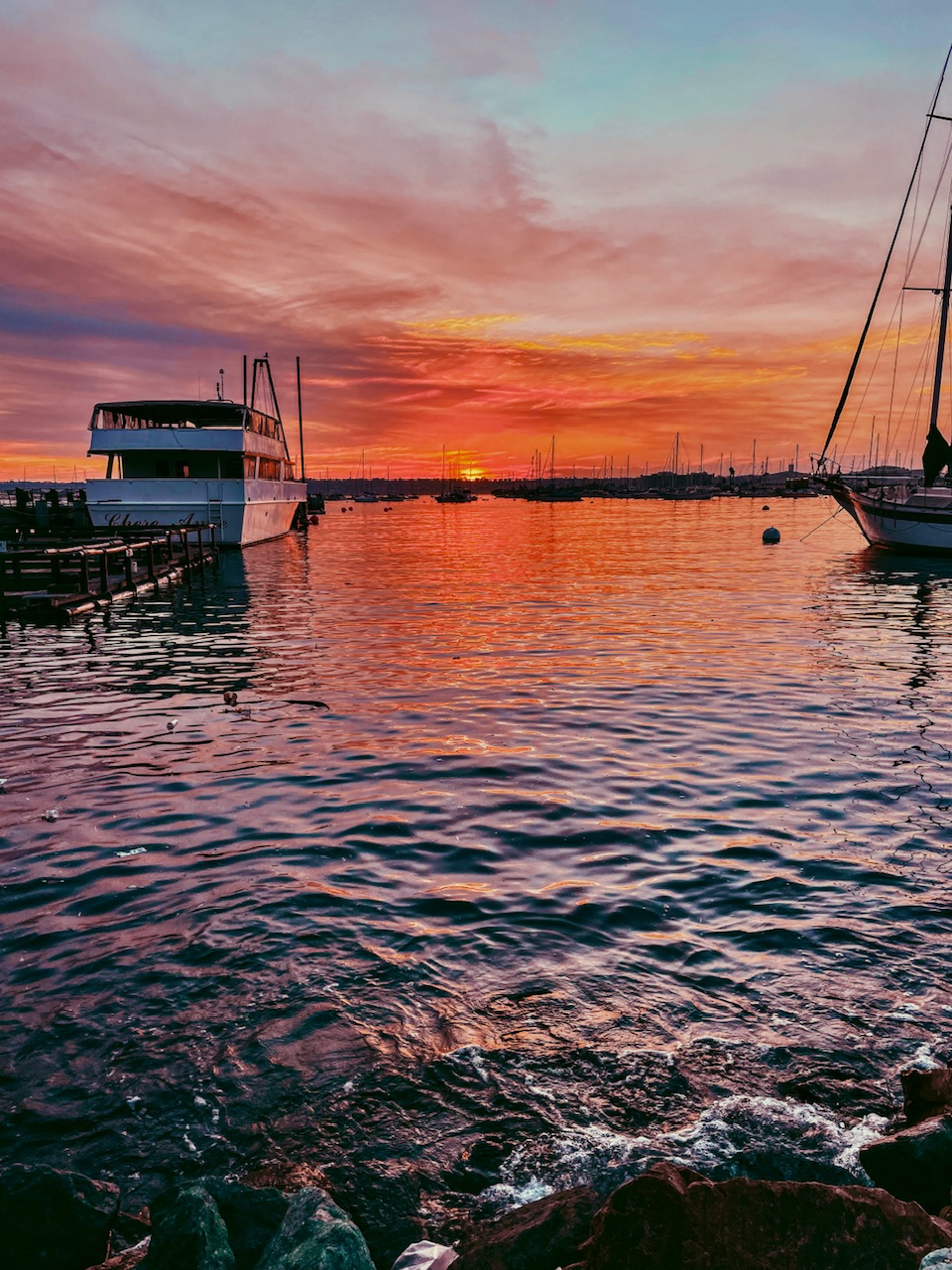 Vibrant red and orange sunset over a calm marina filled with boats and gentle water ripples.